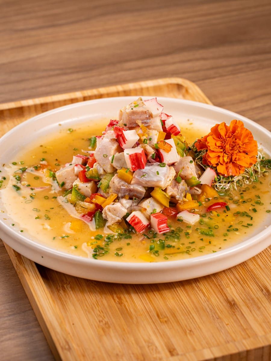Cubos de peixe branco com pimentões coloridos e cebolinha, no caldo cítrico do prato raso