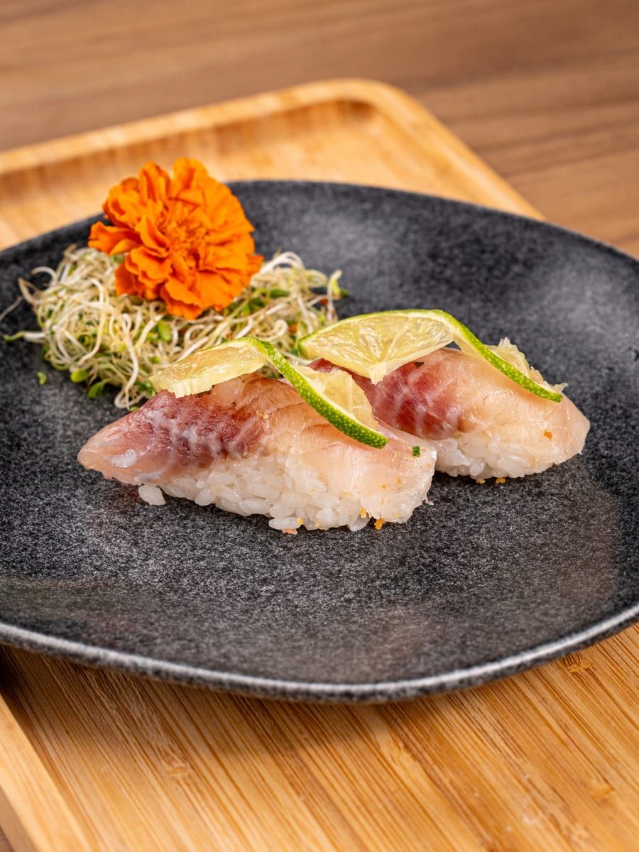 Dois niguiris de peixe branco com rodela de limão, no prato preto