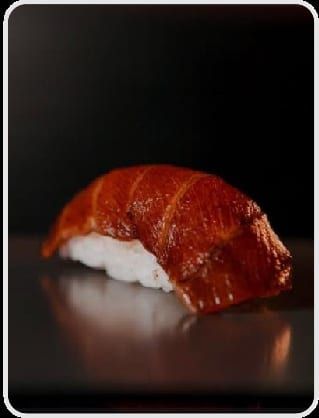 Um niguiri coberto por fatia de salmão curada em molho escuro e brilhante, sobre fundo preto