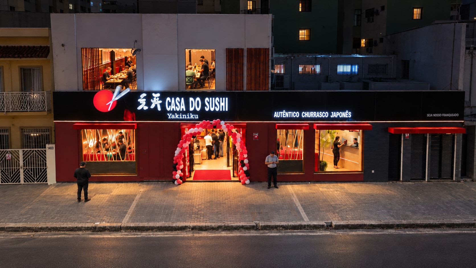 Fachada inteira vista do alto ao anoitecer, com o letreiro aceso, o arco de balões na porta e o salão cheio nas janelas
