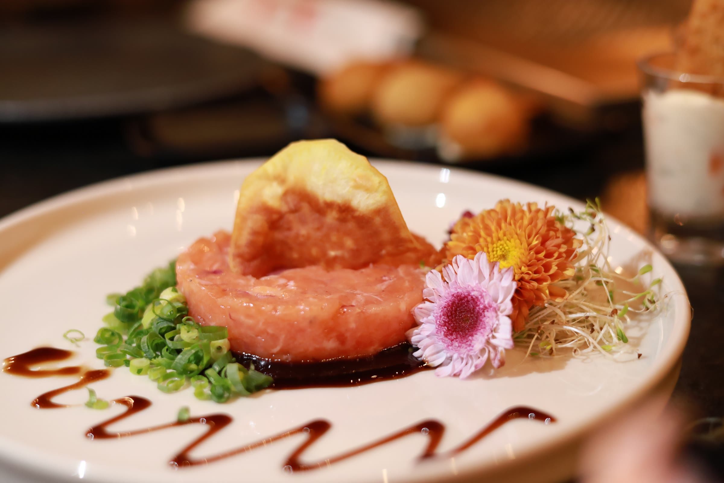 Tartar de salmão com flor comestível e brotos, servido em prato branco