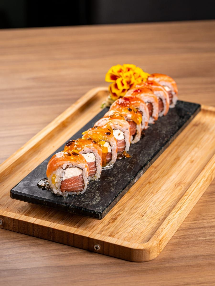 Uramaki especial com fatias de salmão por cima, regado de molho, na ardósia preta