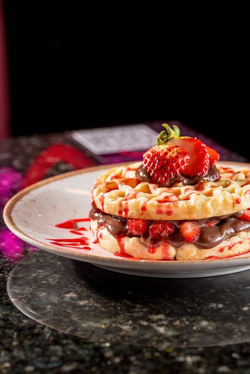 Waffle em duas camadas recheado de creme de chocolate e morangos picados, com um morango inteiro no topo